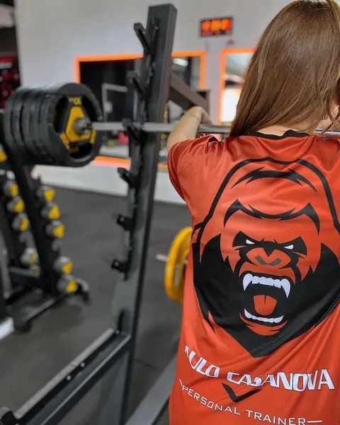 Aluno de costas com a camiseta laranja do Team Casanova, embaixo da barra de agachamento